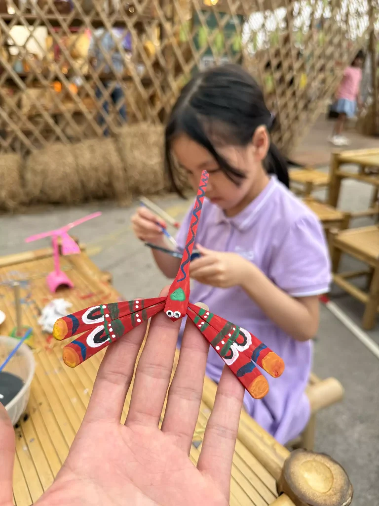 A child at the atelier balancing her freshly painted bamboo dragonfly on a single fingertip